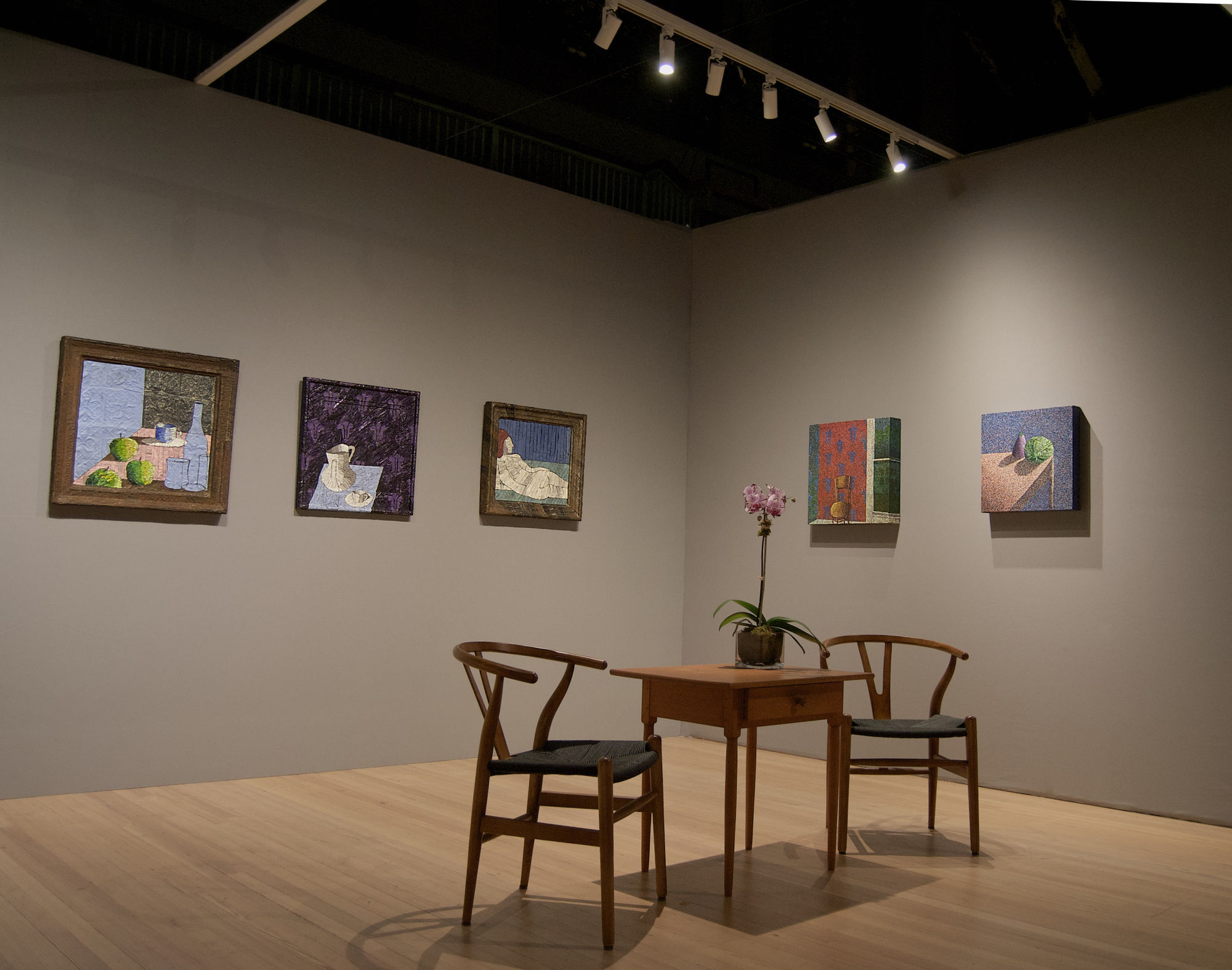 Corner of a room with five paintings, and a table with an orchid sitting on it, and two chairs 