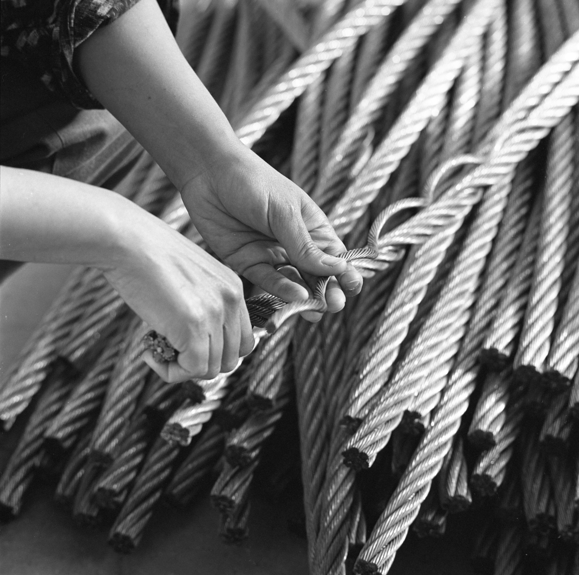 Black and white photograph of hands untwisting thick wire rope 
