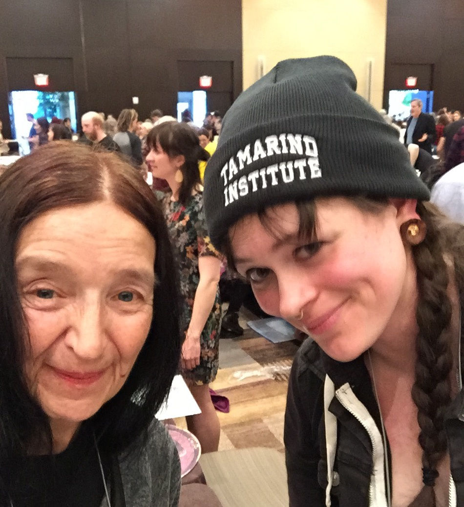 Two artists stand with heads almost touching. The woman on the right wears a hat that reads "Tamarind Institute"