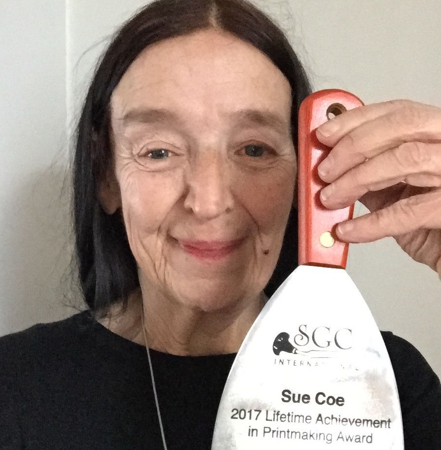 Photograph of the artist Sue Coe holding up an engraved printmaking tool given to her by SGC International
