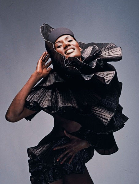 Color photograph of Grace Jones posing with an arm by her face in an all black outfit