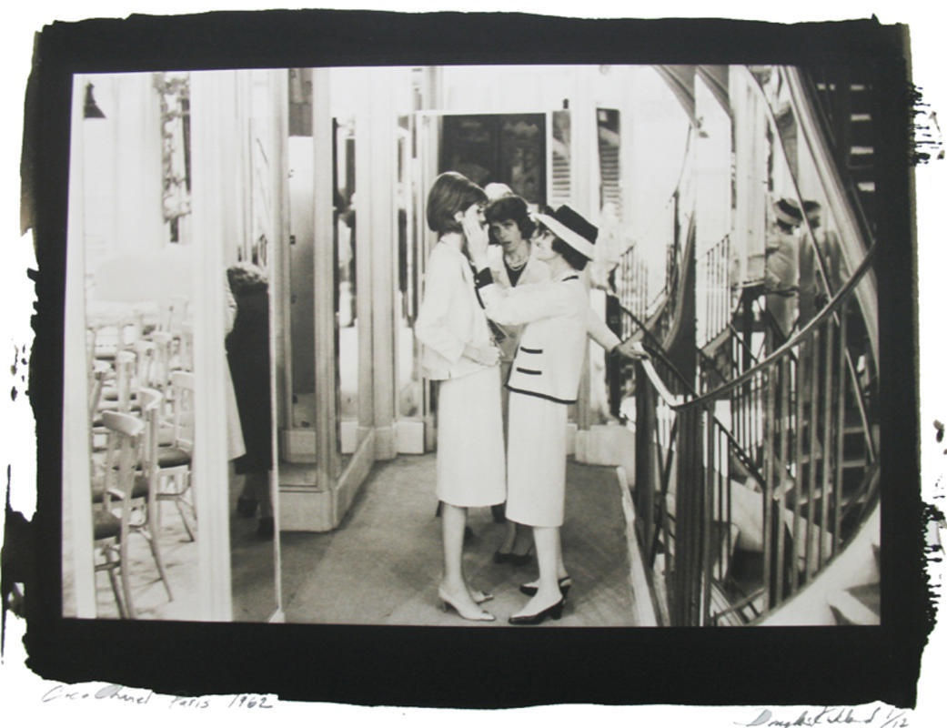 Black and white photograph with black border of Coco Chanel with a model preparing for the new collection on the second floor of House of Chanel in Paris