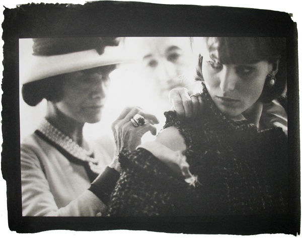 Black and white photograph with black border of Coco Chanel with a model with fitter Jean in background