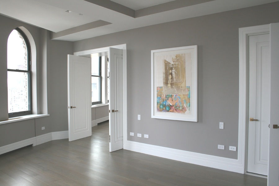 An interior room painted in light beige with dark wood herringbone flooring. Artwork hangs on the walls.