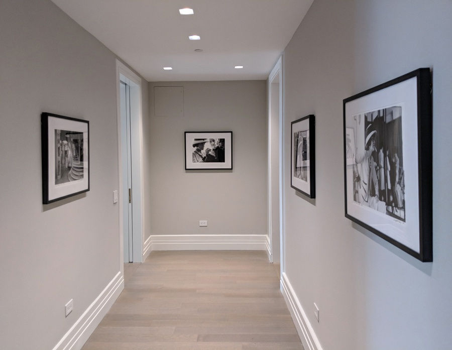 An interior room painted in light beige with dark wood herringbone flooring. Photography of Coco Chanel hangs on the walls.