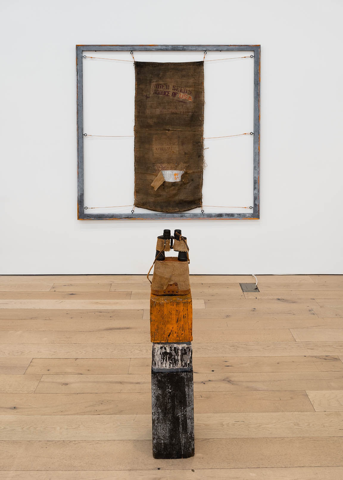 Jared Owens Panopticon, 2021 Painting: Burlap pig feed sack, acrylic, steel cable, steel eye hooks, silk screen printing, soil from FCI Fairton prison yard. Plinth: Reclaimed dunnage, silk screen printing, acrylic, binoculars, burlap. 70 x 70 inches 42 x 7 1/2 x 7 1/2 inches (base)