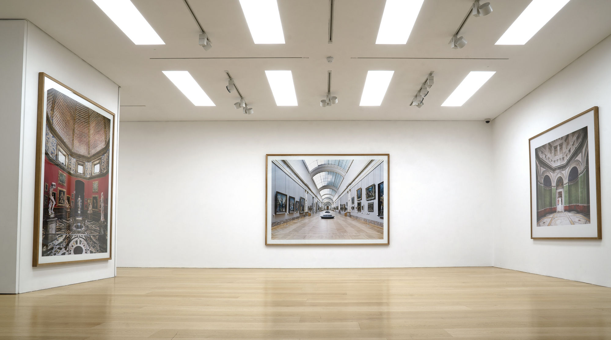 Installation view of a white cube gallery with wooden floors showing large scale framed photographs of interiors by Candida Hofer
