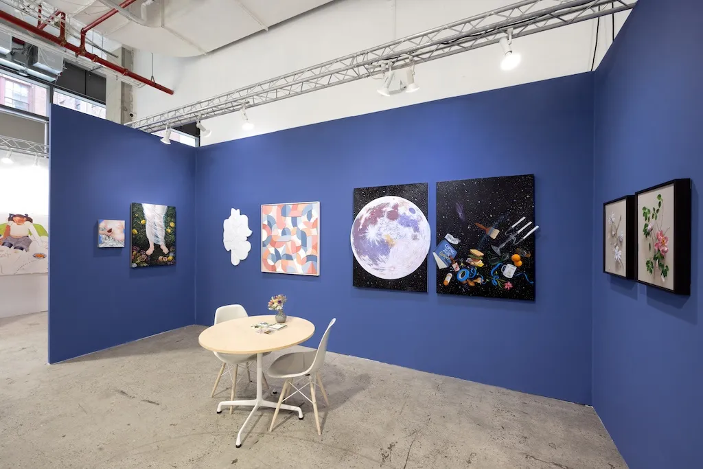 blue booth with various artworks hanging on walls. round table to the left
