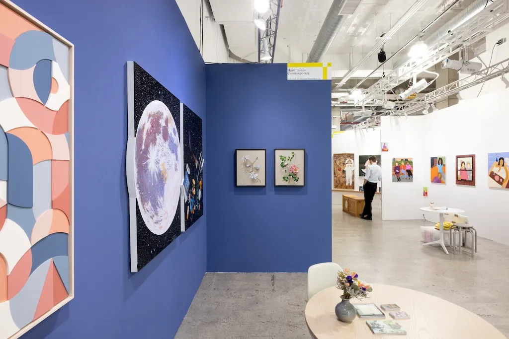 blue booth with various artworks hanging on walls. round table in foreground