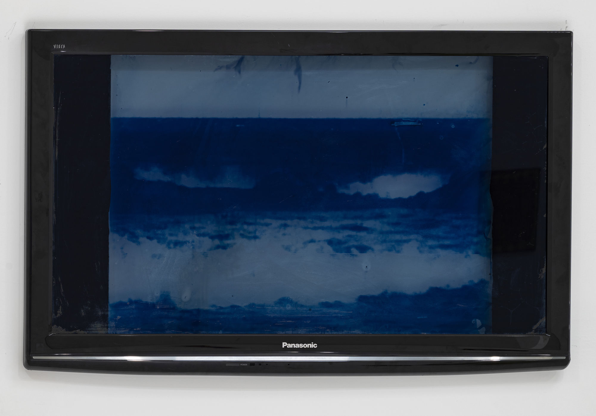 Africanus Okokon for every tortured geography, 2025 Cyanotype and silkscreen on found Panasonic Viera TC-P46S1 glass with found Panasonic Viera TC-P46S1 bezel 26 1/2 x 40 x 1 1/2 inches 67 x 101 x 3 cm