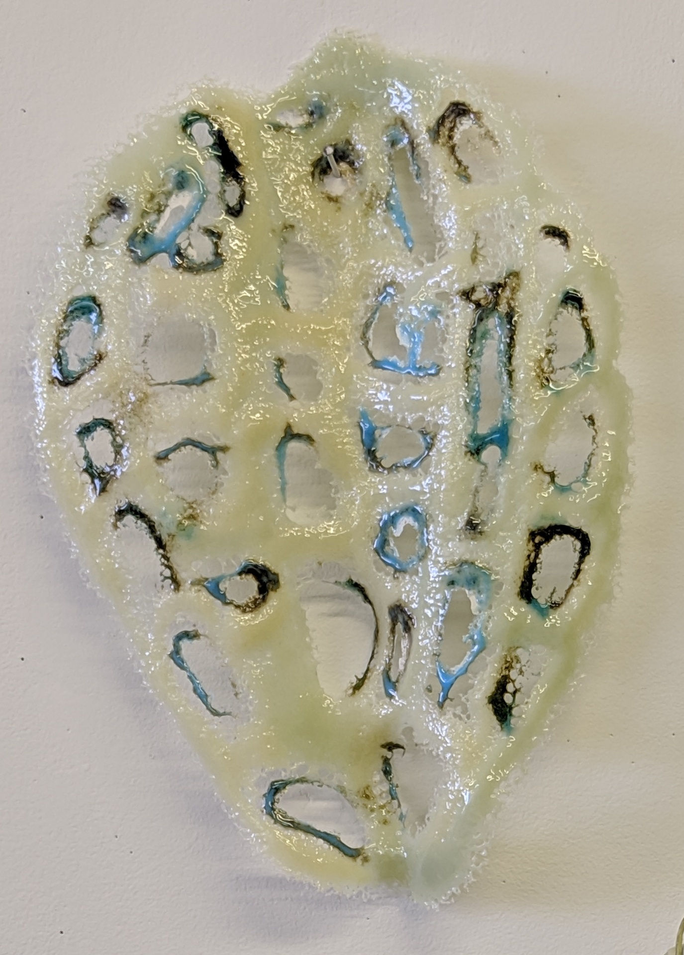 Nancy Cohen's "Diffusion" art piece made entirely out of glass. The glass has small streaks of black and blue around the holes. These holes on the glass is creating an asymmetrical pattern.