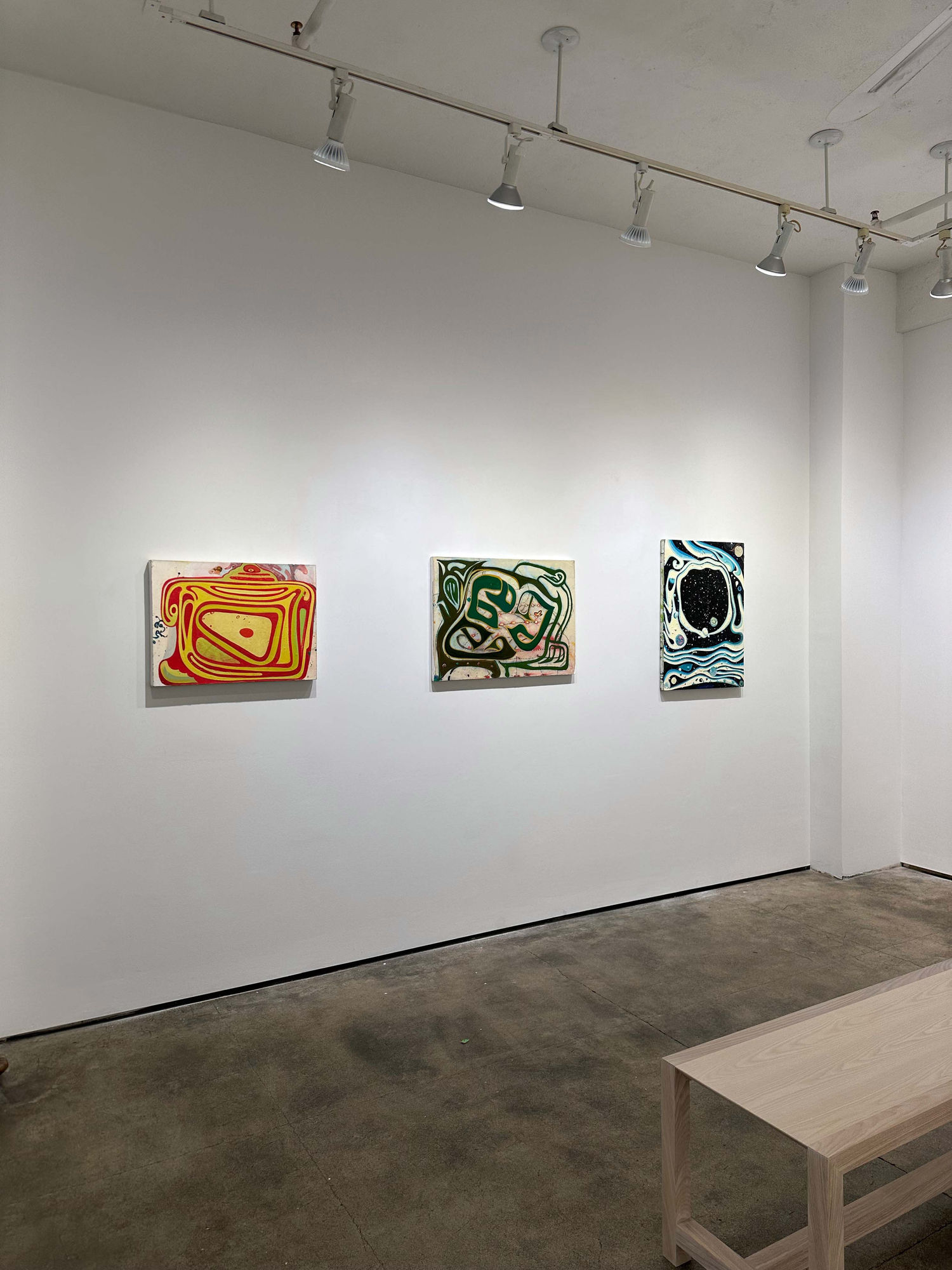 exhibition with three paintings on a wall. there is a bench peeking into the foreground 