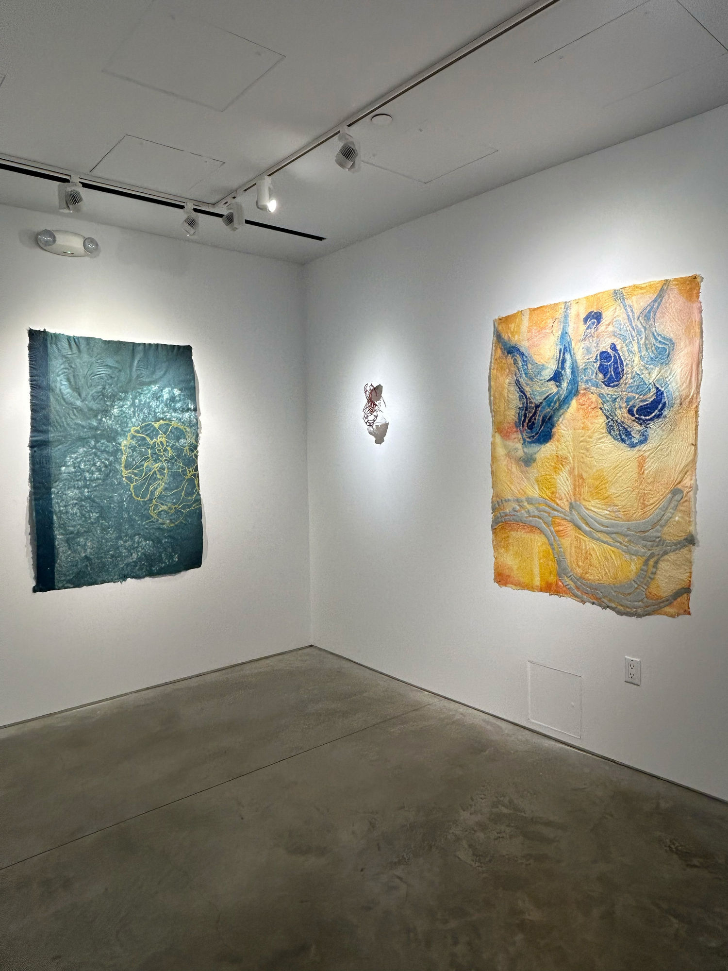 photo of an installation with two large works, and one small sculpture between them. the leftmost work is blue, and the rightmost is primarily orange.