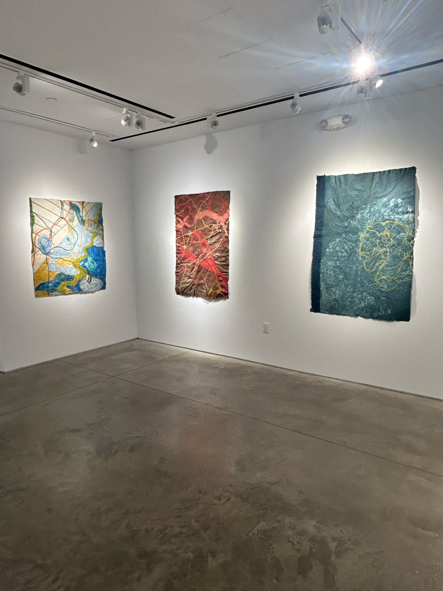 photo of an installation with three large works on paper on the walls. From left to right, they are mostly white, red, and blue