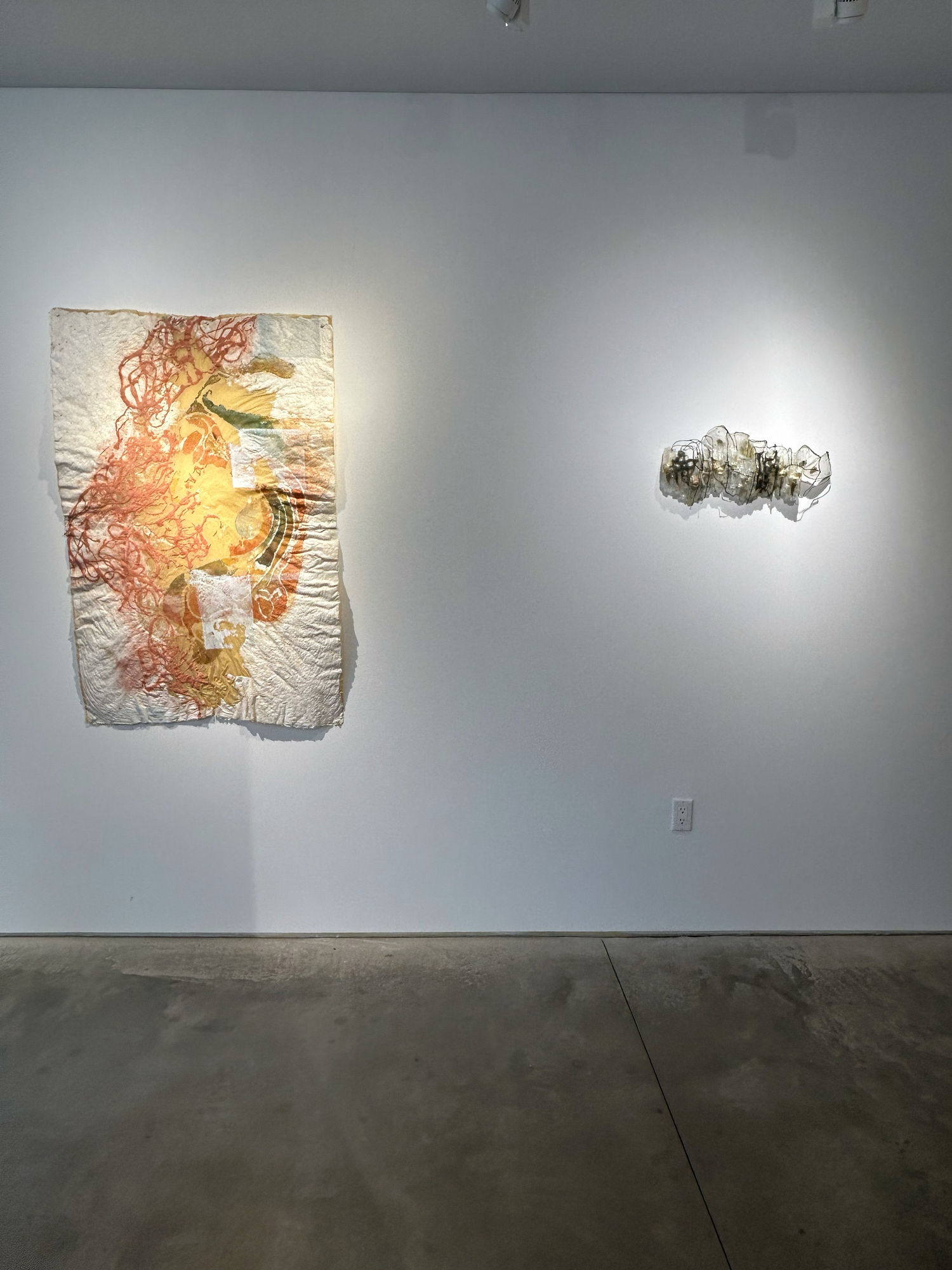 photo of an installation with one large work on paper hanging next to a small sculpture, which are both on the wall.
