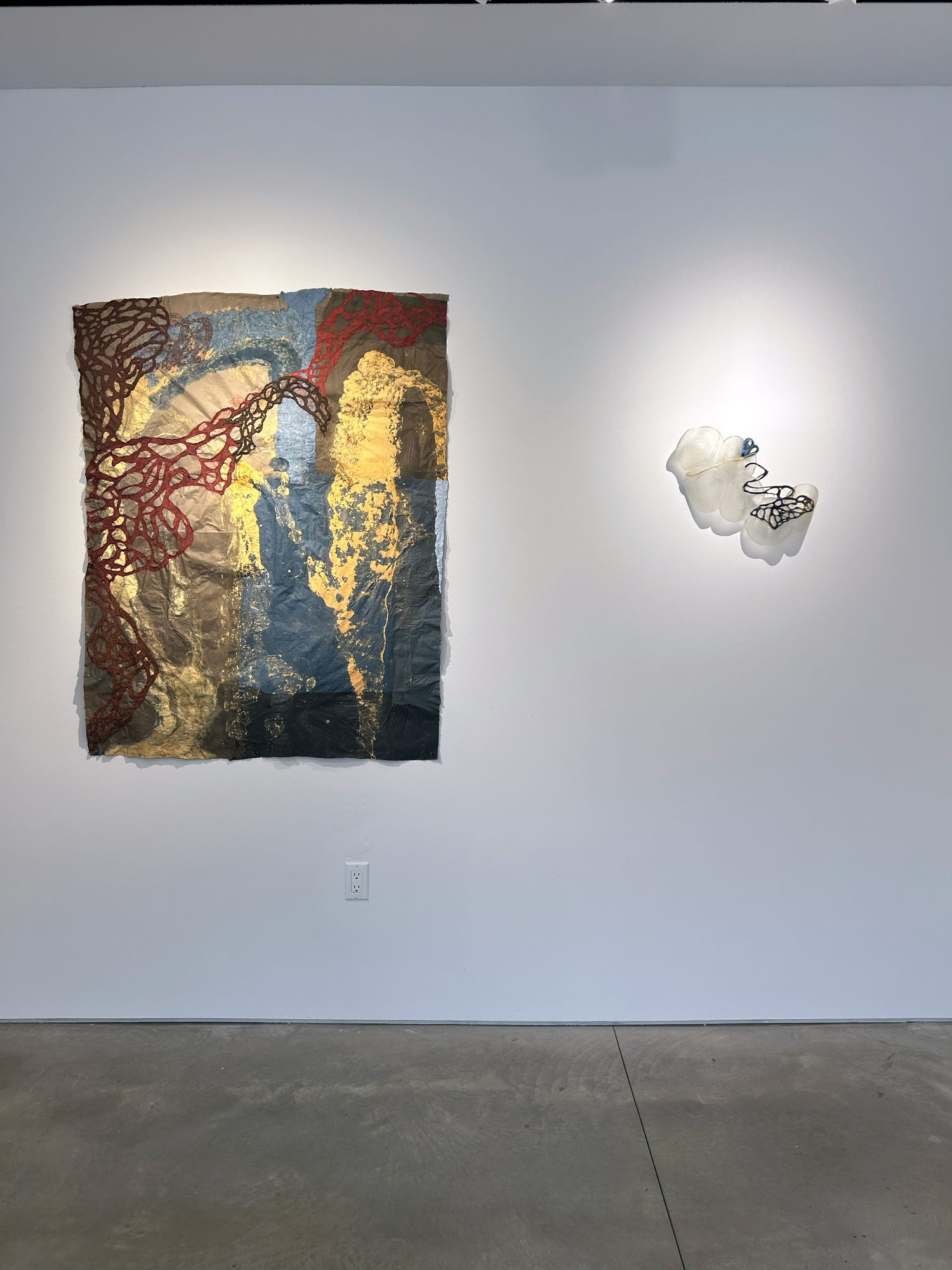 photo of an installation with one large work on paper hanging next to a small sculpture. Both are on the wall.