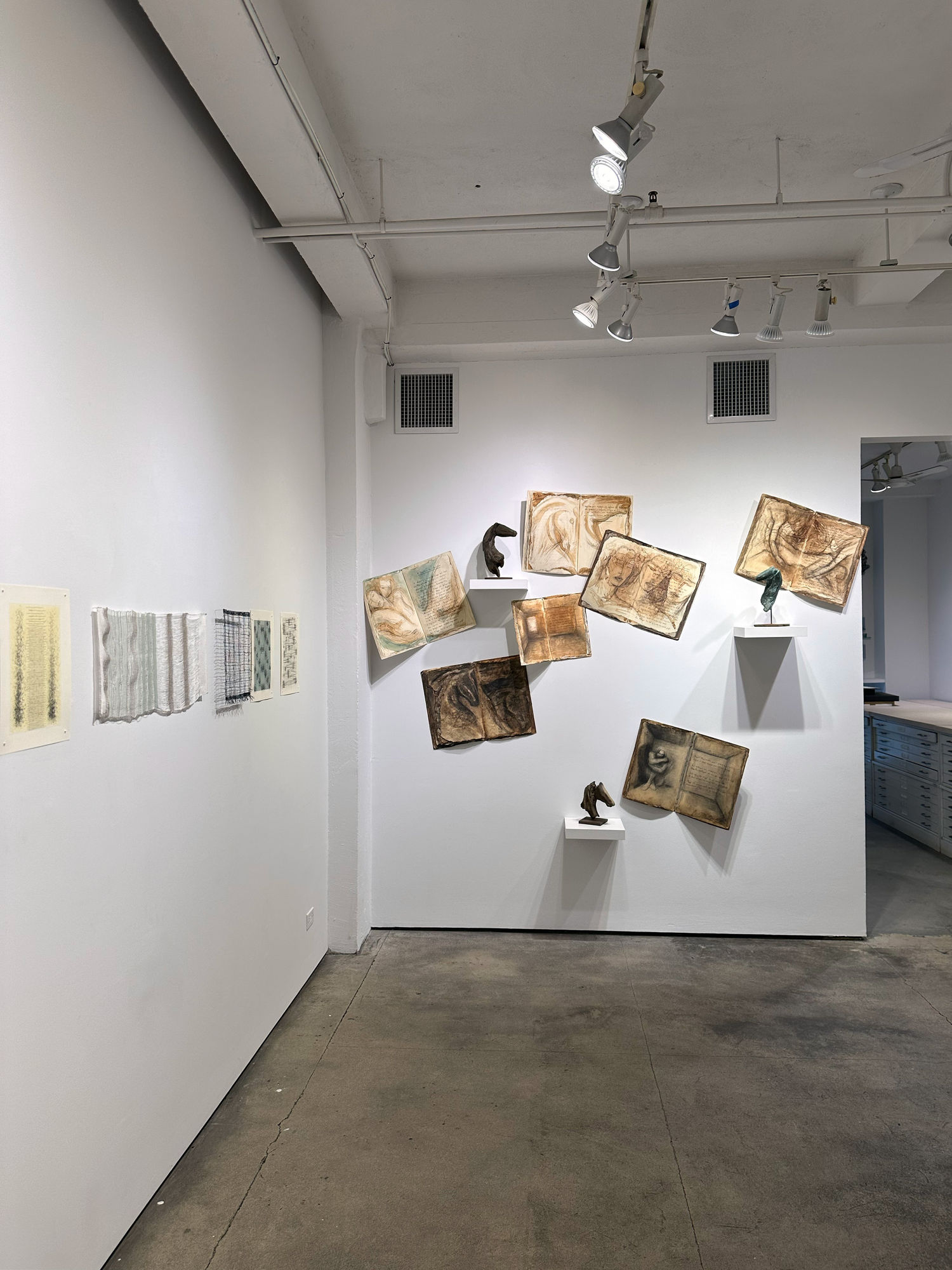 photo of an installation with two page spreads placed irregular on the wall. There are drawings over the text on the pages.