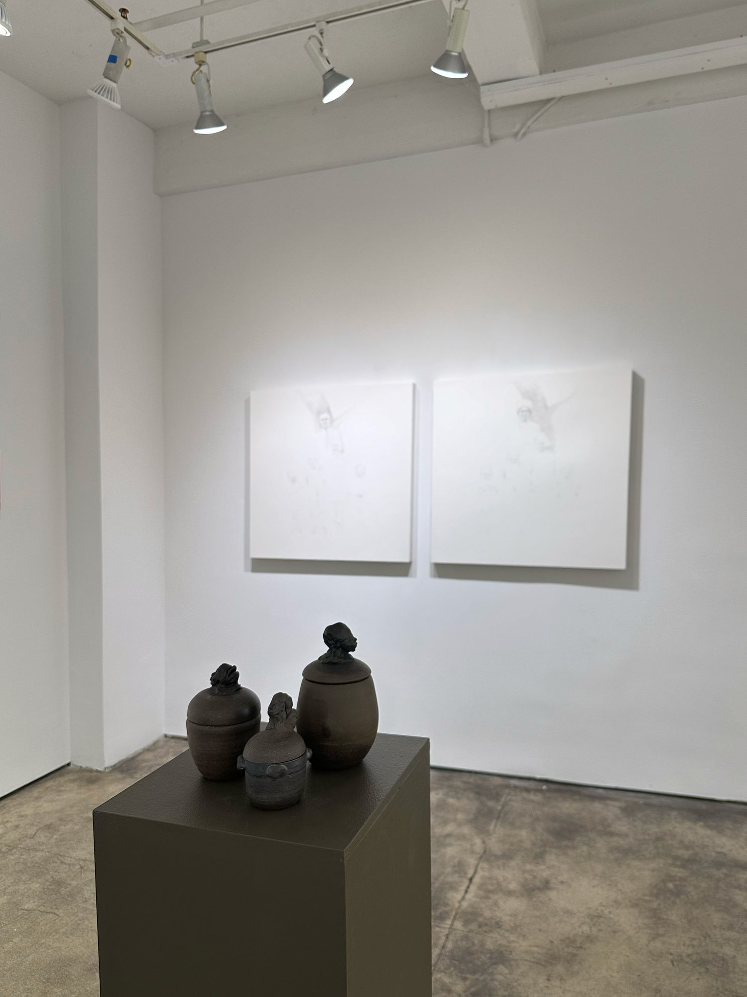 photo of an installation with three small urns on a pedestal. behind them on the wall are two primarily white paintings.