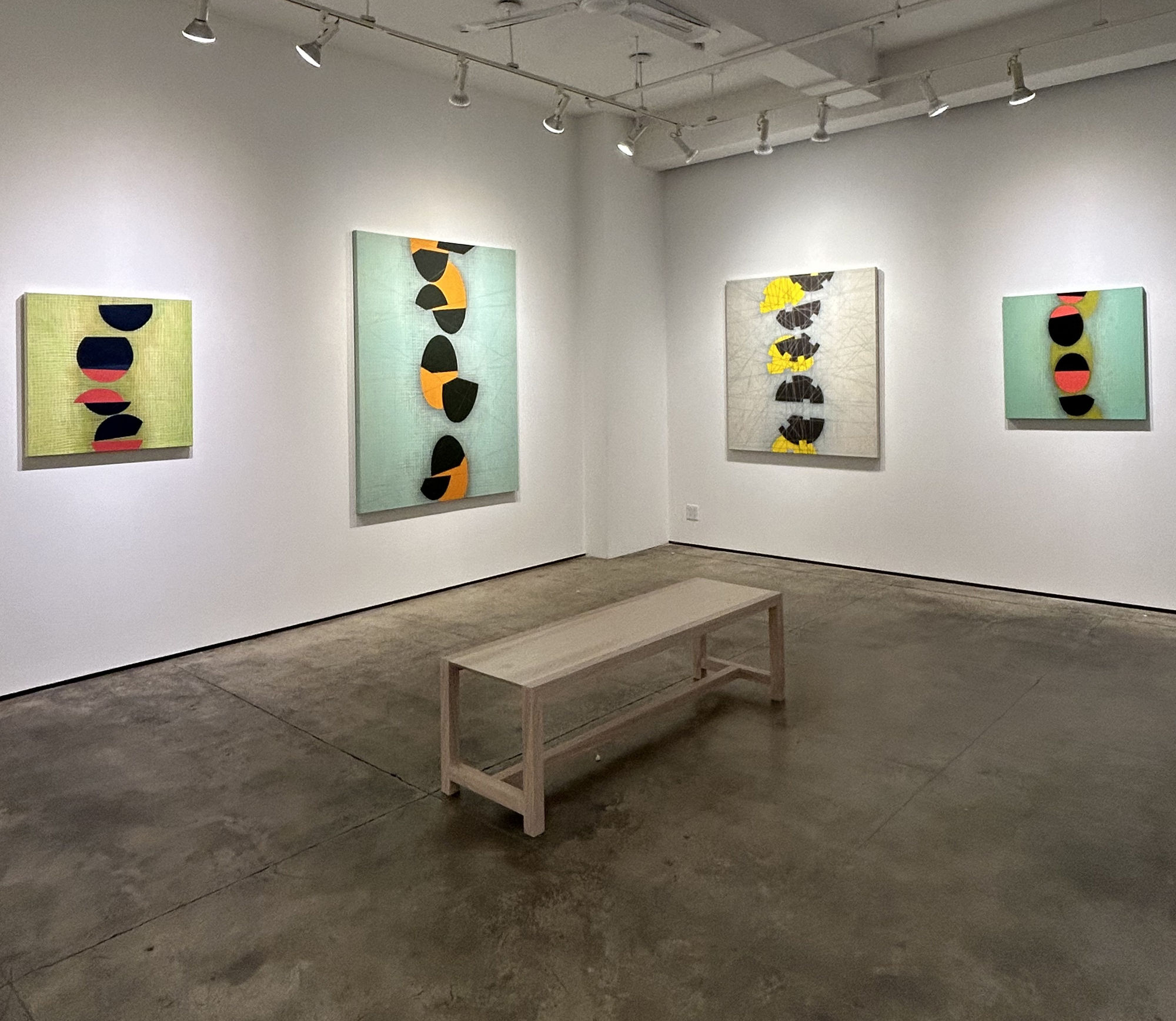 Photo of a Steve Baris exhibition, called Stations of Attention. There are four paintings visible on the walls, and a bench in the center of the room. Each painting has a low contrast painted grid in the background, with a series of circular shapes going 