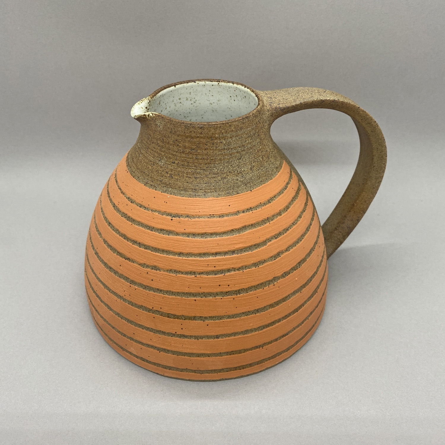 Kate Garwood brown jug in a round shape with an orange body and horizontal stripes.