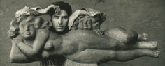 Black and white photo of Chaim Gross with a sculpture. The wood sculpture depicts a nude woman figure laying on her side with a small child's head and body resting behind her on her hips and legs. Chaim Gross is standing behind the sculpture, resting his arms on it and looking straight ahead.