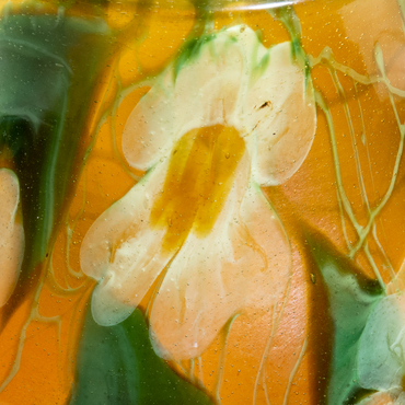 a detail shot of an authentic tiffany favrile glass paperweight vase, depicting white flowers against an iridescent amber background with pointed green leaves and swirling thin green vines