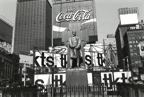 Black and white photo of the Father Duffy statue in Times Square with a cluster of advertising signage behind.