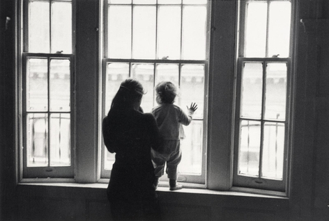 Black and white image showing a mother and child in silhouette as they look at out a city window.
