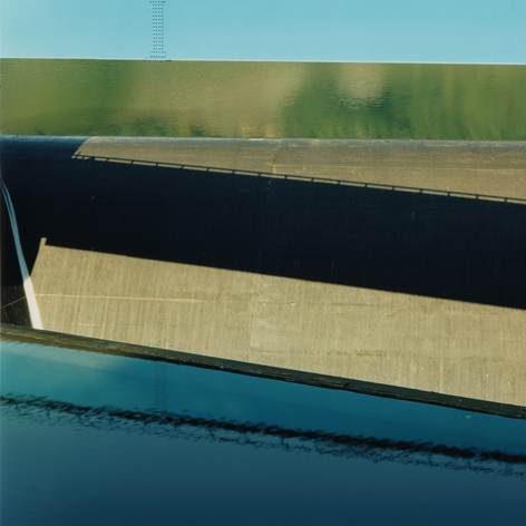 Abstracted color photograph a waterway, dam, and bridge, showing reflections on water.