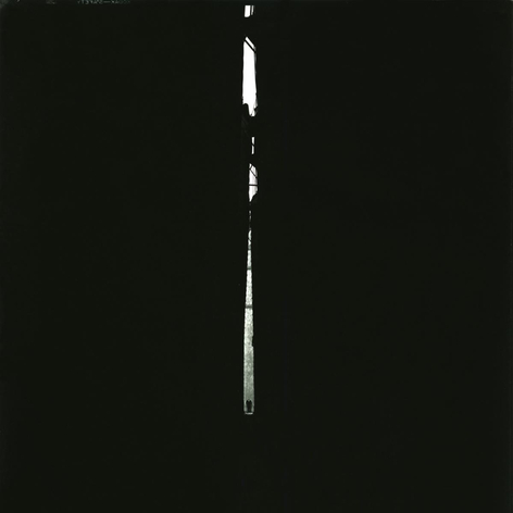 Stark black and white photo showing a man in a suit seen at great distance in a shaft of light, with a large expanse of darkness on each side.