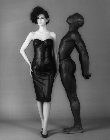 Black and white image of white woman with strapless dress and black male in a thong