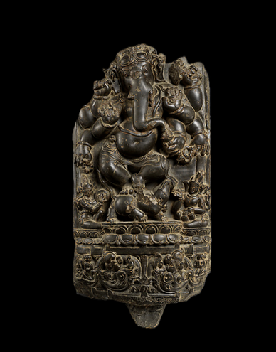 This finely-carved stone relief depicts Ganesha, the elephant-headed son of Shiva, dancing in a compact yet animated posture within a vertically-framed niche.