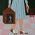 Angela Burson painting of torso and legs - woman in blue dress holding calico cat in brown cage. Pink tiled floor