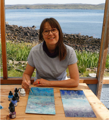 Catherine Sargeant painting in a coastal studio setting with art supplies.