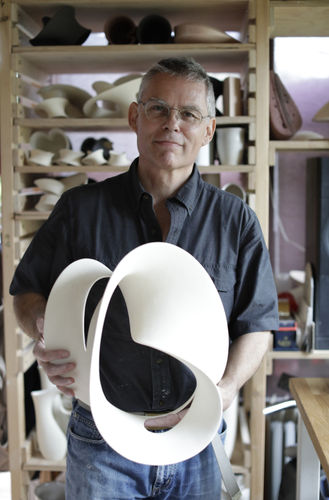 Person holding a contemporary white ceramic sculpture in a workshop.