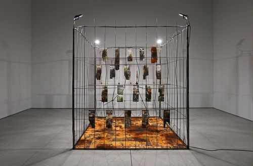 Marcin Dudek, Sektor, 2021, Steel fence, jesmonite, ash, resin, textile, medical tape, acrylic paint, image transfer, wood, uv varnish, flood lights. 240 x 210 x 210 cm - 94 1/2 x 82 5/8 x 82 5/8 in. Courtesy of Galerie Ron Mandos and Harlan Levey Projects