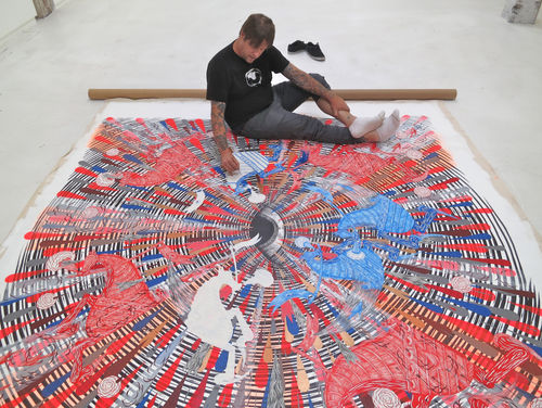 Andrew schoultz sitting on unstretched painting he is working on