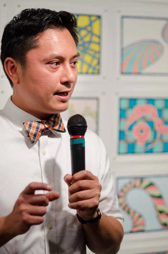 Lordy Rodriguez stands in front of wall of his drawings. He is speaking with microphone