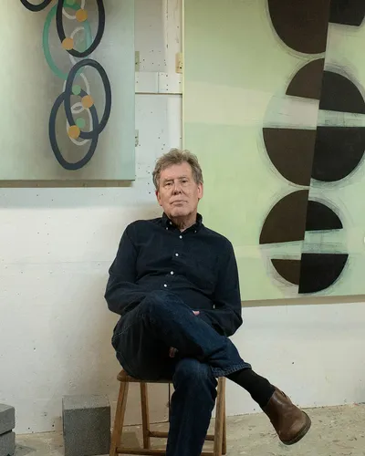 Steven Baris sitting in his studio among some of his abstract paintings.