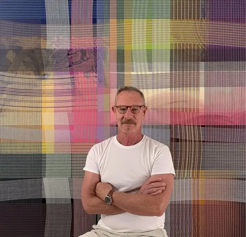 Peter Stephens sitting in front of one of his paintings.