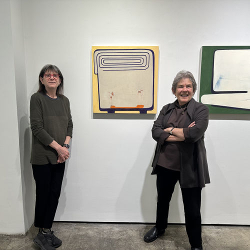 Two woman standing in front of a gallery wall with two abstract paintings.