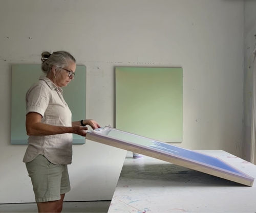Woman standing in her art studio holding a canvas with dripping paint