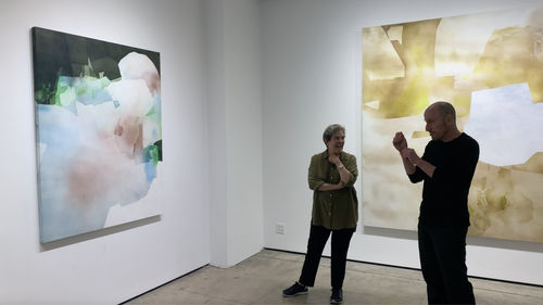 Kathryn Markel and artist Eric Blum in gallery with 2 of his abstract paintings.