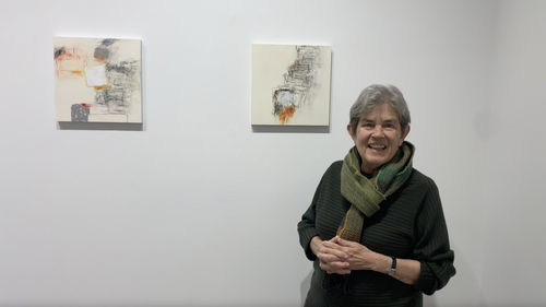 Woman standing in front of two small abstract paintings on a gallery wall.