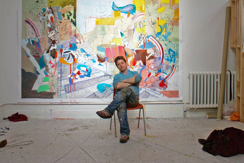 Alejandro Ospina artists photo, artist sitting in his studio, backgrounded by one of his works.