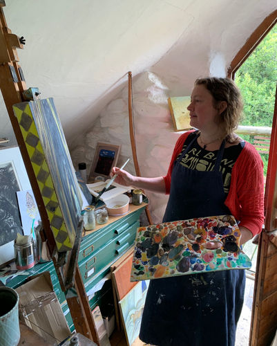 Flora McLachlan shown in front of an easel, holding a brush and a palette.