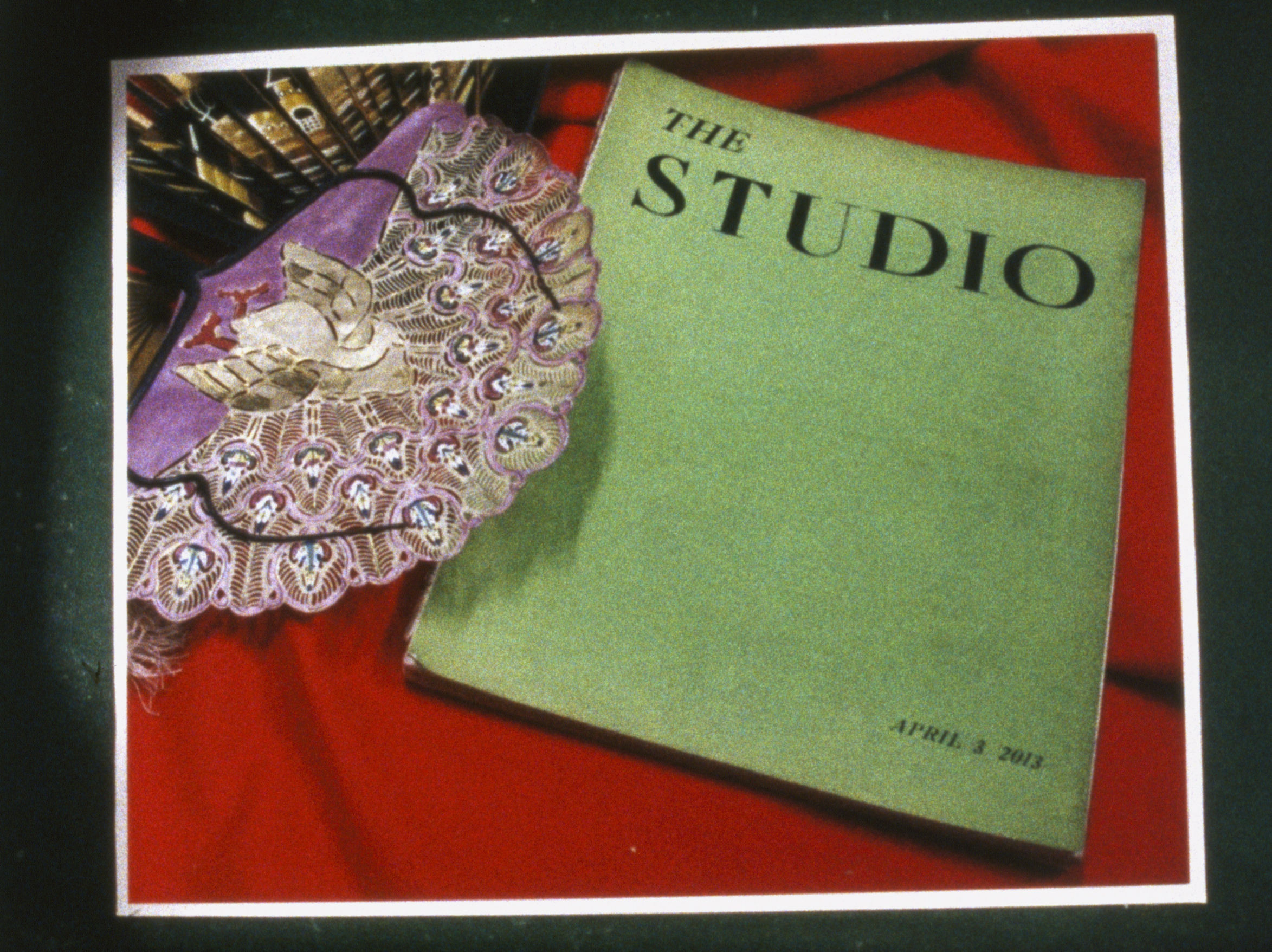 on a red tablecloth, a green booklet titled In the Studio next to a pink decorative mask 