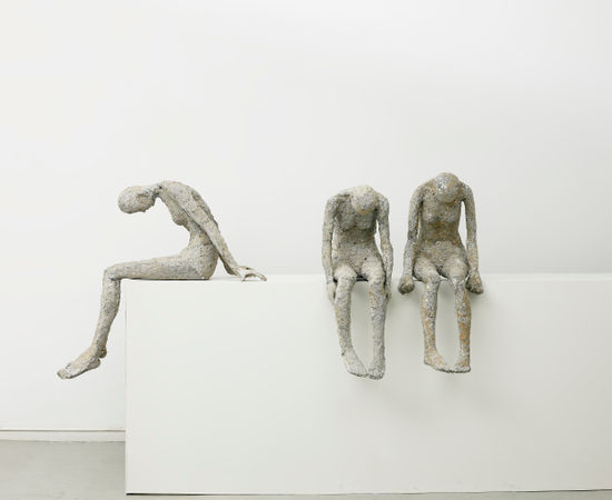 Three women sit on a white table with their heads bent. 