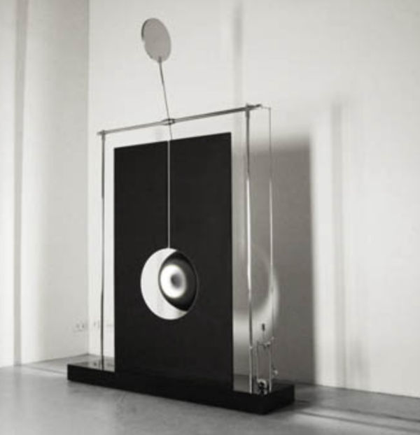 A kinetic sculpture by Damien Bénéteau featuring a suspended black sphere rotating in front of a light disc, framed by stainless steel structure. Title: Spatial Variations, 2012.