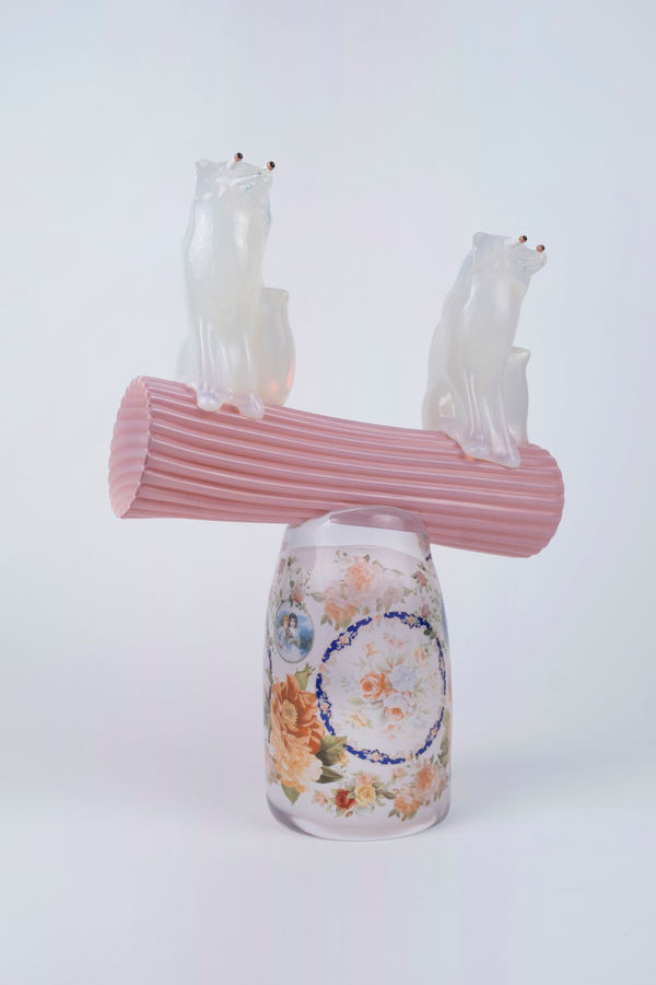 Rasmus Nossbring glasskulptur med två rävar i opalin vitt sittande på en rosa pelare som balanserar på en glasdekal med blommor.